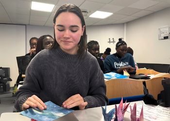 Jeune femme brune étudiante de l'ESGRH dans une salle de classe fabrique des origamis en papier