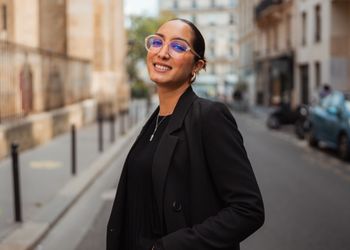 Jeune femme brune en tenue professionnelle avec des lunettes dans les rues de Paris regarde la caméra 