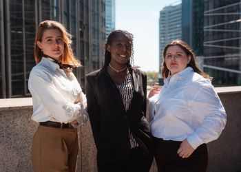 Trois étudiantes debout sourient face caméra