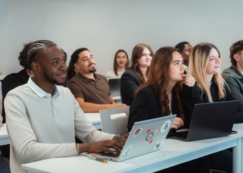 Une salle de classe avec des élèves assis à leur table avec dessus des ordinateurs et qui sourient face caméra