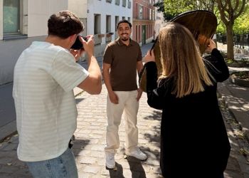 En extérieur au premier plan de dos un photographe et une responsable de communication ajuste la luminosité pour un étudiant au second plan souriant et face caméra