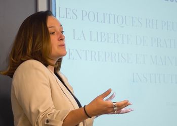 Femme brune en tenue professionnelle devant un tableau dans une salle de classe