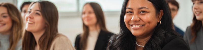 Femme brune dans une salle de classe avec des étudiants sourit à la caméra Femme brune dans une salle de classe avec des étudiants sourit à la caméra
