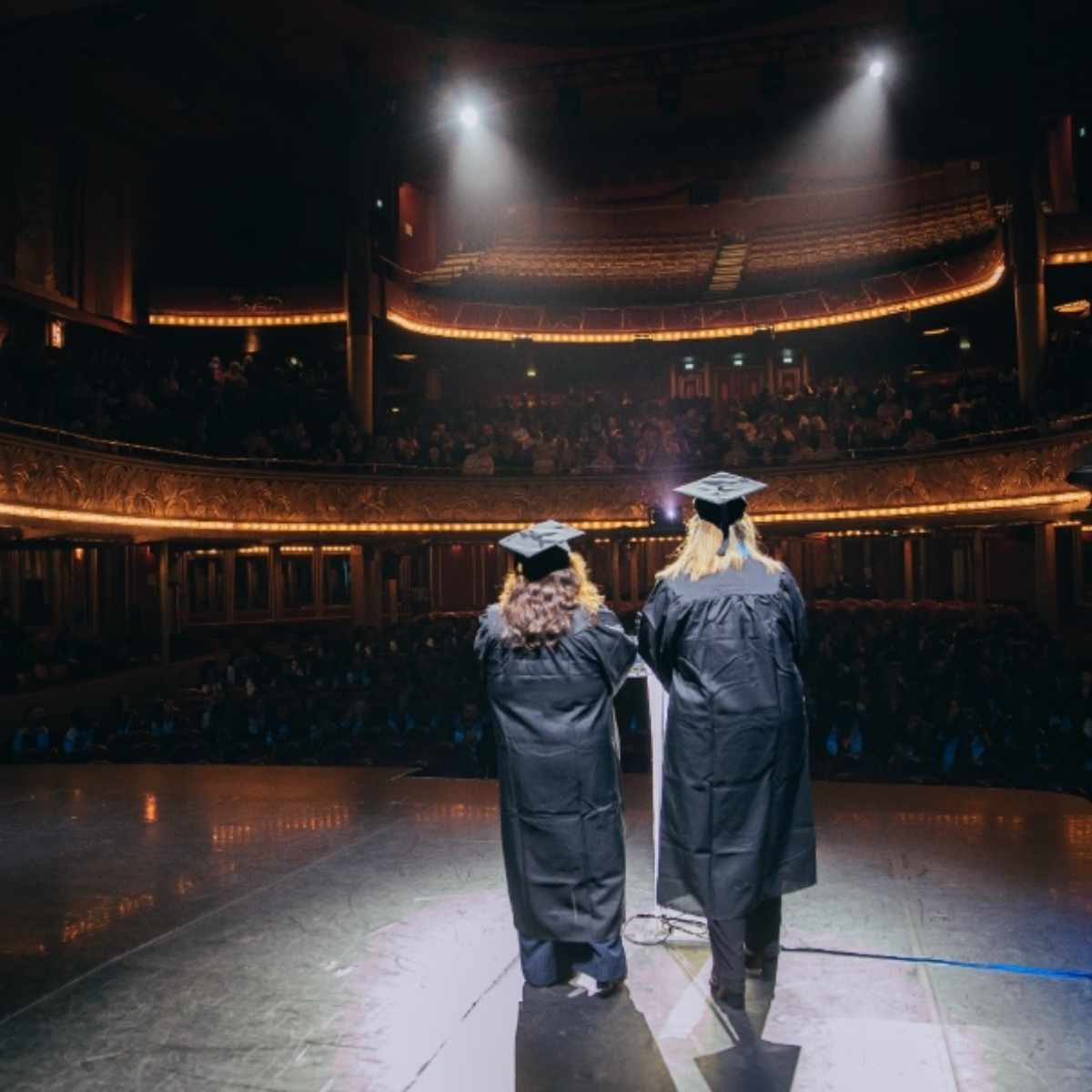 Deux étudiantes sur scène sont debout et dos à la caméra et face au public