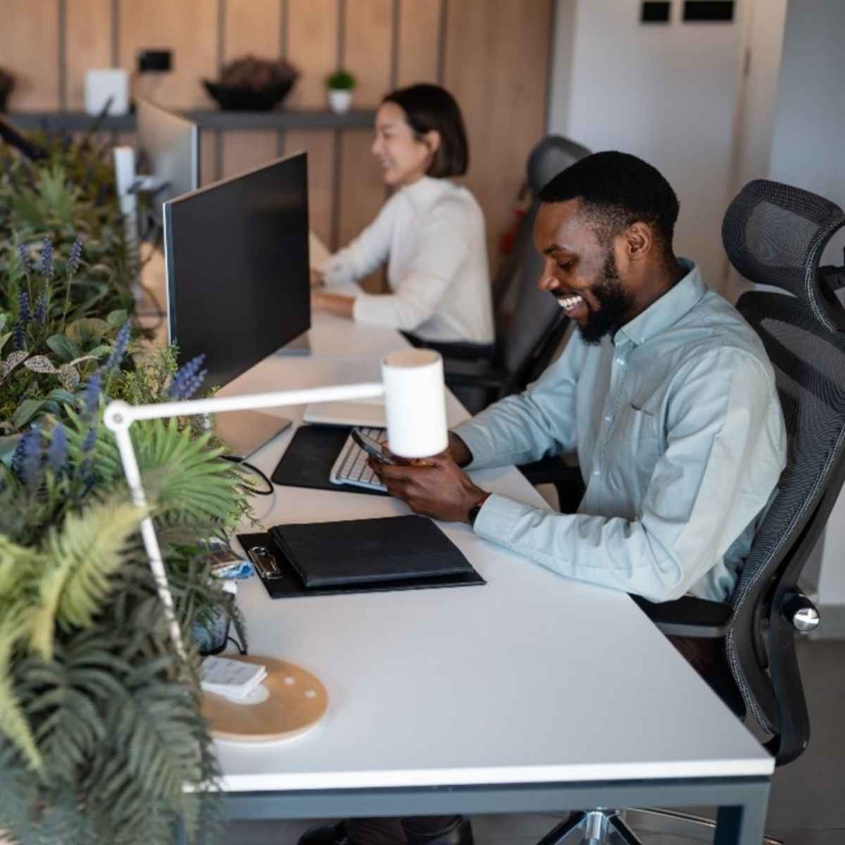 1 homme au premier plan est assis à son bureau et une femme au second plan également