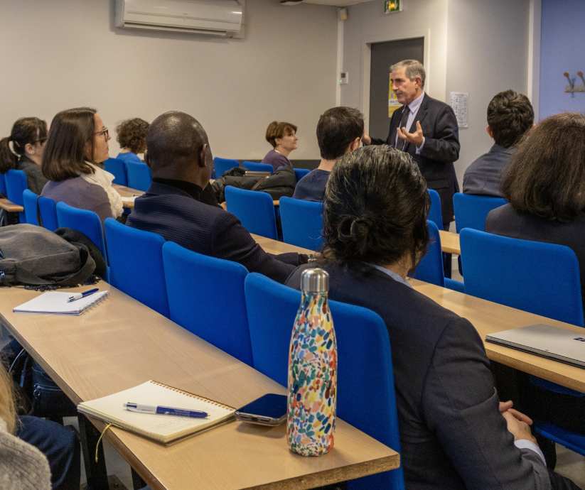 Homme costume noir et cheveux blancs, donne une conférence à étudiants assis sur chaises bleues